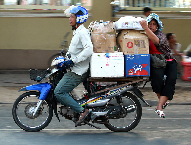 A motorcycle 'taxi' driver transports a trader and dry goods to the Phnom Penh market. Phnom Penh,